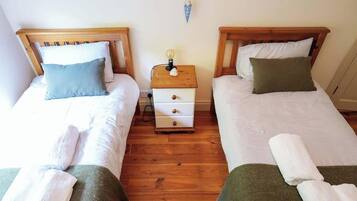 A room with two single beds, a wooden nightstand with a lamp, and a wall-mounted light fixture.