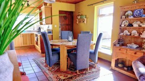 Un coin repas avec une table et des chaises en bois, une cuisine en arrière-plan et une étagère remplie de vaisselle.