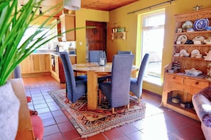 Un comedor con una mesa y sillas de madera, una cocina al fondo y una alacena con vajilla.