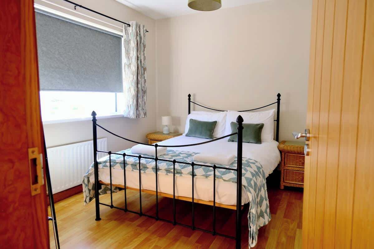 Um quarto com estrutura de cama de metal, uma mesa de cabeceira, uma janela com cortina e um radiador.