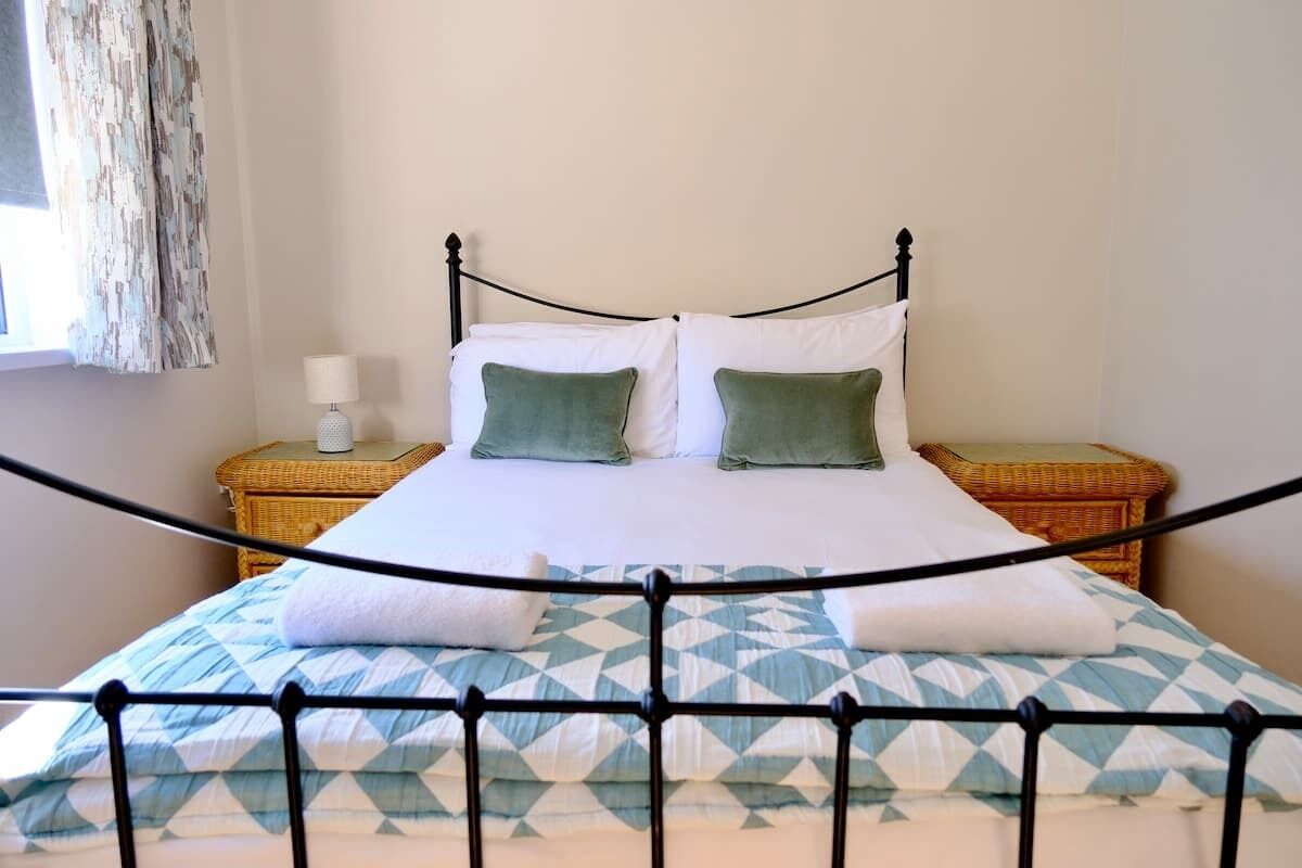 Una cama con estructura metálica, dos almohadas, sábana blanca y edredón estampado.