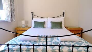 Una cama con estructura metálica, dos almohadas, sábana blanca y edredón estampado.