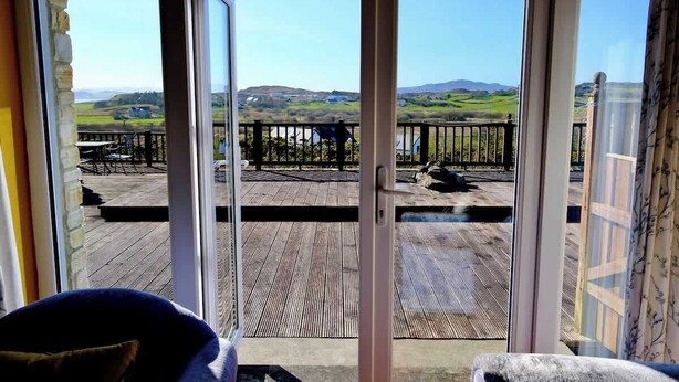 Une pièce dotée d’une grande porte-fenêtre coulissante qui donne sur une terrasse extérieure offrant une vue sur des collines verdoyantes.