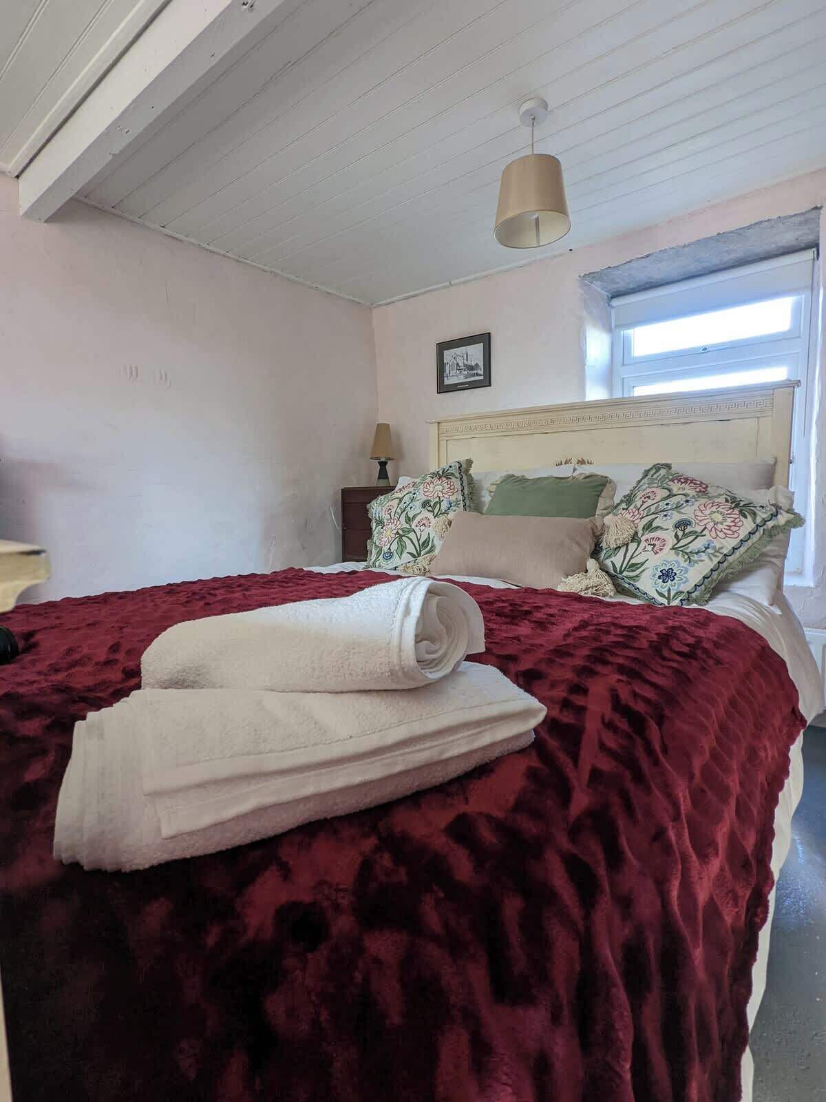 Une chambre à coucher avec un lit, une table de chevet, une lampe, une fenêtre et un luminaire au plafond.
