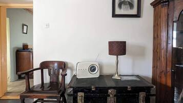 Um quarto com uma cadeira de madeira, um rádio antigo, uma luminária e um baú.