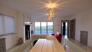 Une pièce spacieuse avec une grande table, un canapé rouge, un lustre original et une vue magnifique à travers de grandes fenêtres.