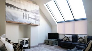 Un salon de style industriel, avec une verrière, un téléviseur, un canapé et un tableau accroché au mur.