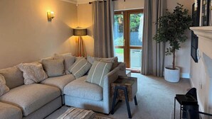 A living room with a sectional sofa, a small side table, a lamp, a potted plant, and a fireplace. - Modern 4 Bed,3 Bath Detached Home with Sea View (Quigley's Point)
