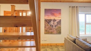 Une pièce avec un plafond en bois, un tableau représentant un paysage encadré, un canapé et une fenêtre avec des rideaux.