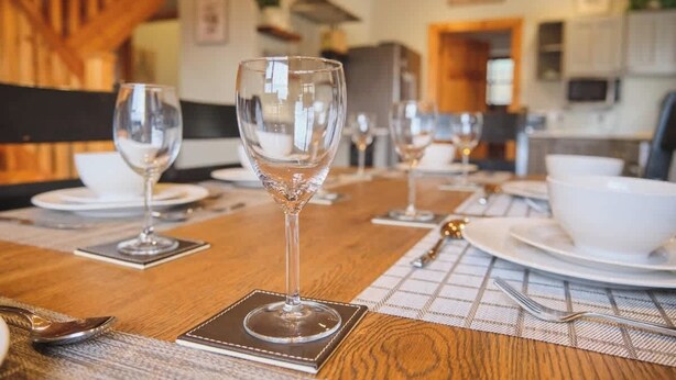 Une table à manger dressée avec des verres à vin, des assiettes et des couverts, sur une table en bois et agrémentée d’un set de table à carreaux.
