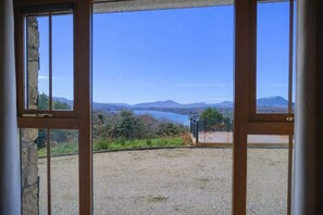 A view through a window with a gravel ground and a distant body of water, surrounded by hills.