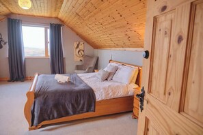 A bedroom with a wooden ceiling, a bed with a grey blanket, a chair, and a wardrobe.