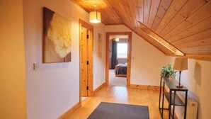 Un couloir avec un plancher en bois, un tapis gris, un lit à l’arrière-plan et une plante sur une table.