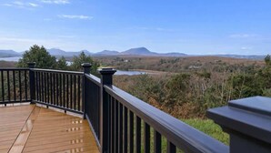 Une terrasse en bois avec une rambarde noire donnant sur un paysage de montagnes et d’un lac.