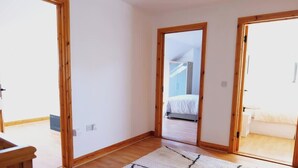 A room with wooden flooring, a white wall, and a door leading to another room. - 4BR Workers Accommodation | Sleeps 7 | Wi-Fi (Letterkenny)