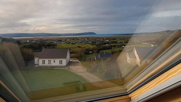 Een kamer met een groot raam met uitzicht op een landschap met huizen en verre heuvels.