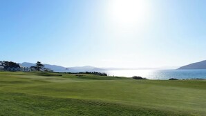Um campo de golfe com vista para o mar e montanhas.