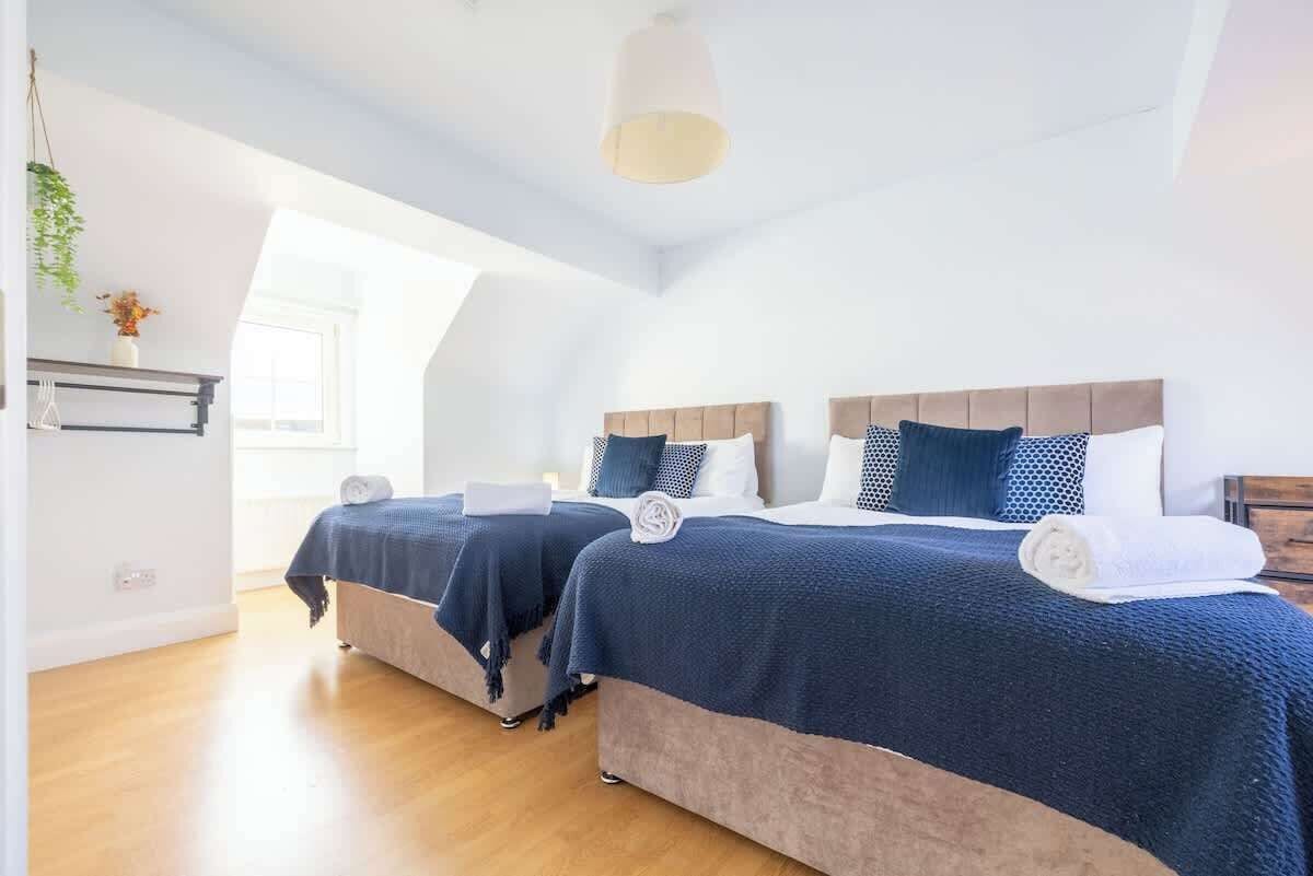 A room with two beds, a hanging plant, a window, and a ceiling light.
