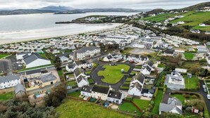 Un quartier résidentiel situé sur la côte, avec des maisons, un espace vert central et une étendue d’eau.