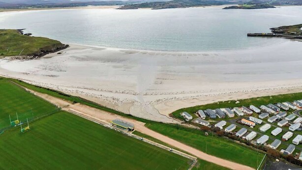Une zone côtière dotée d’une plage de sable, d’un port de plaisance et d’une rangée de maisons mobiles.
