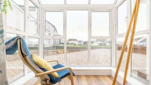 Une véranda avec une chaise en bois, de grandes fenêtres et une vue sur un quartier résidentiel.