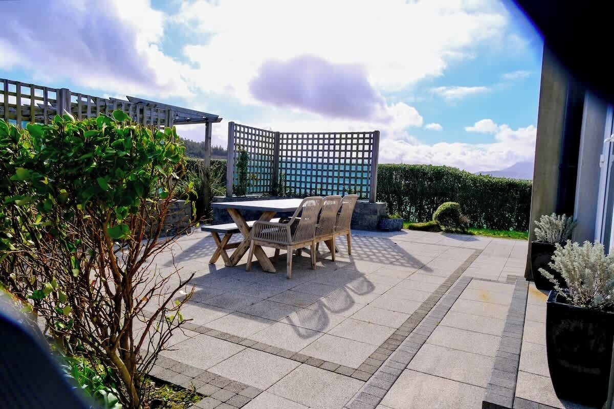 Une terrasse extérieure avec une table et des chaises, une pergola et une haie.