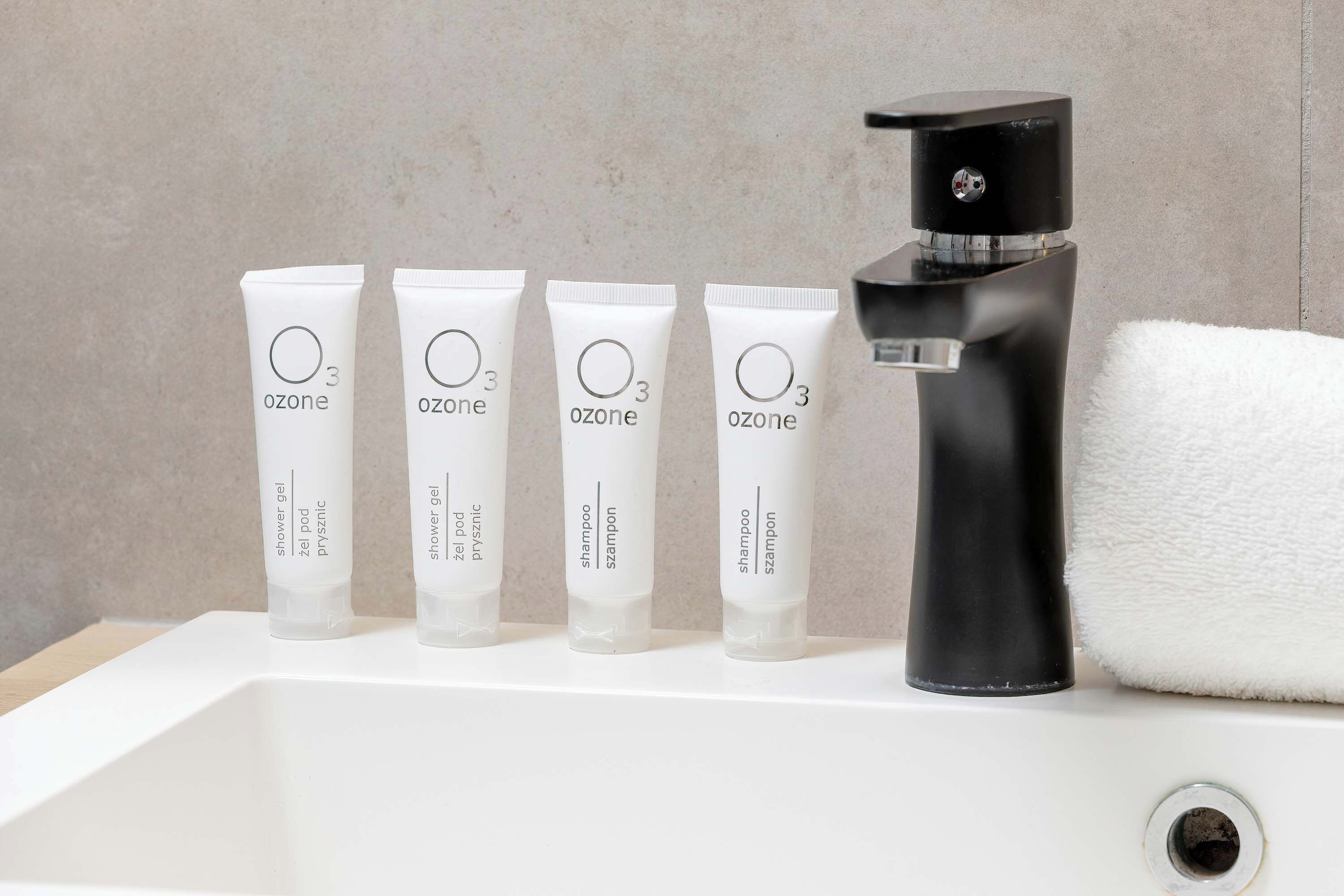 Cuatro tubos de gel de ducha Ozone y dos tubos de champú Ozone sobre un lavabo blanco con un grifo negro.