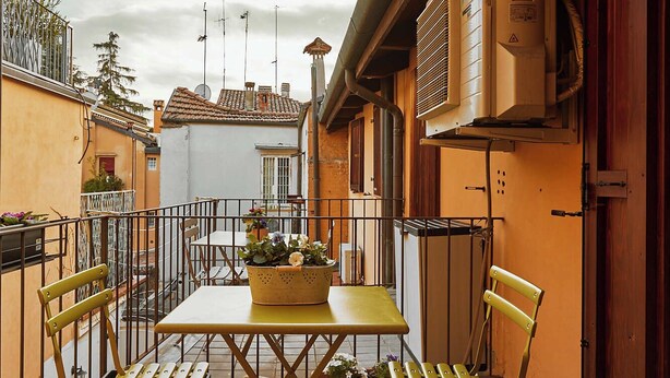 Une terrasse extérieure avec une table et des chaises, un pot de fleurs et une vue sur les bâtiments voisins.
