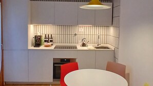 Une cuisine moderne avec un plan de travail blanc, une suspension jaune et une table de salle à manger ronde, assortie de chaises.