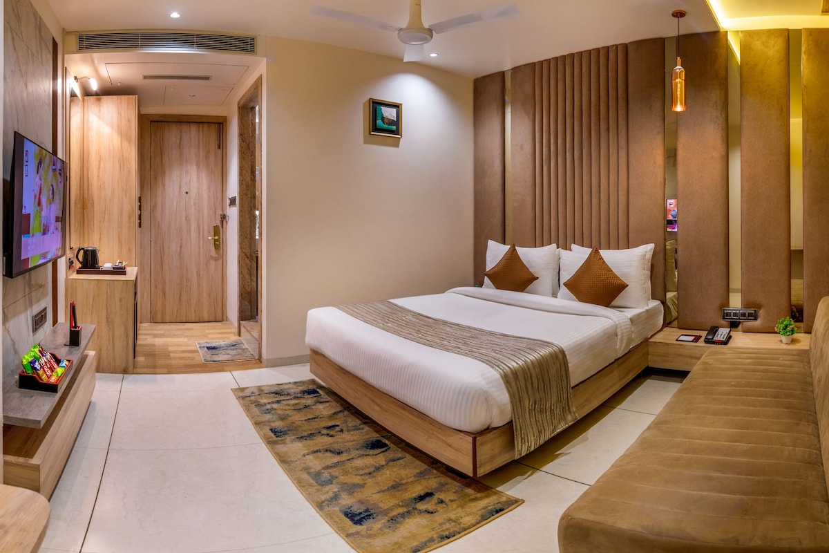 Una habitación de hotel moderna con una cama grande, televisión, escritorio y sofá.