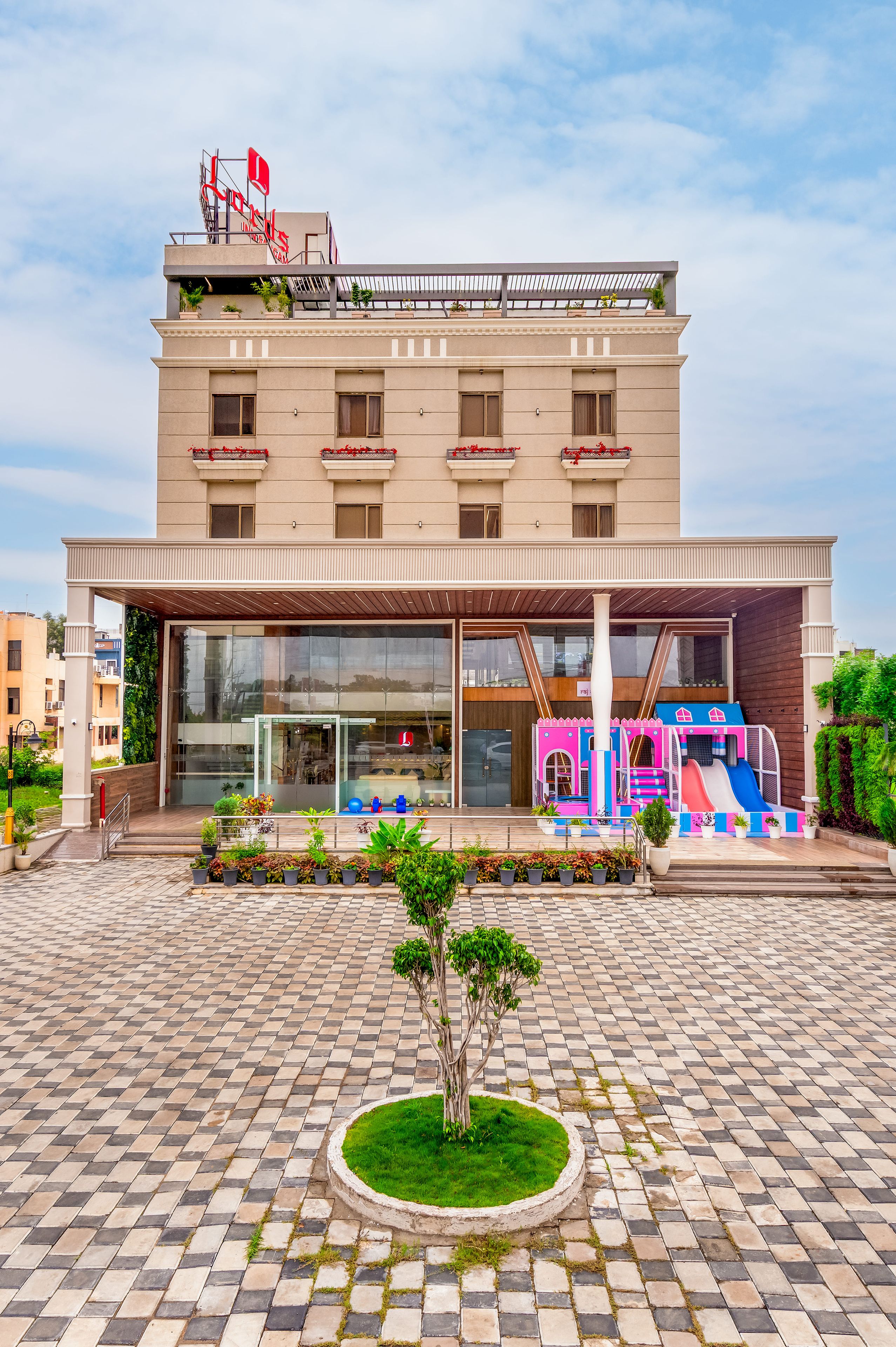 Un hôtel à plusieurs étages doté d’une entrée couverte, d’un espace de jeux pour enfants et d’un petit jardin.