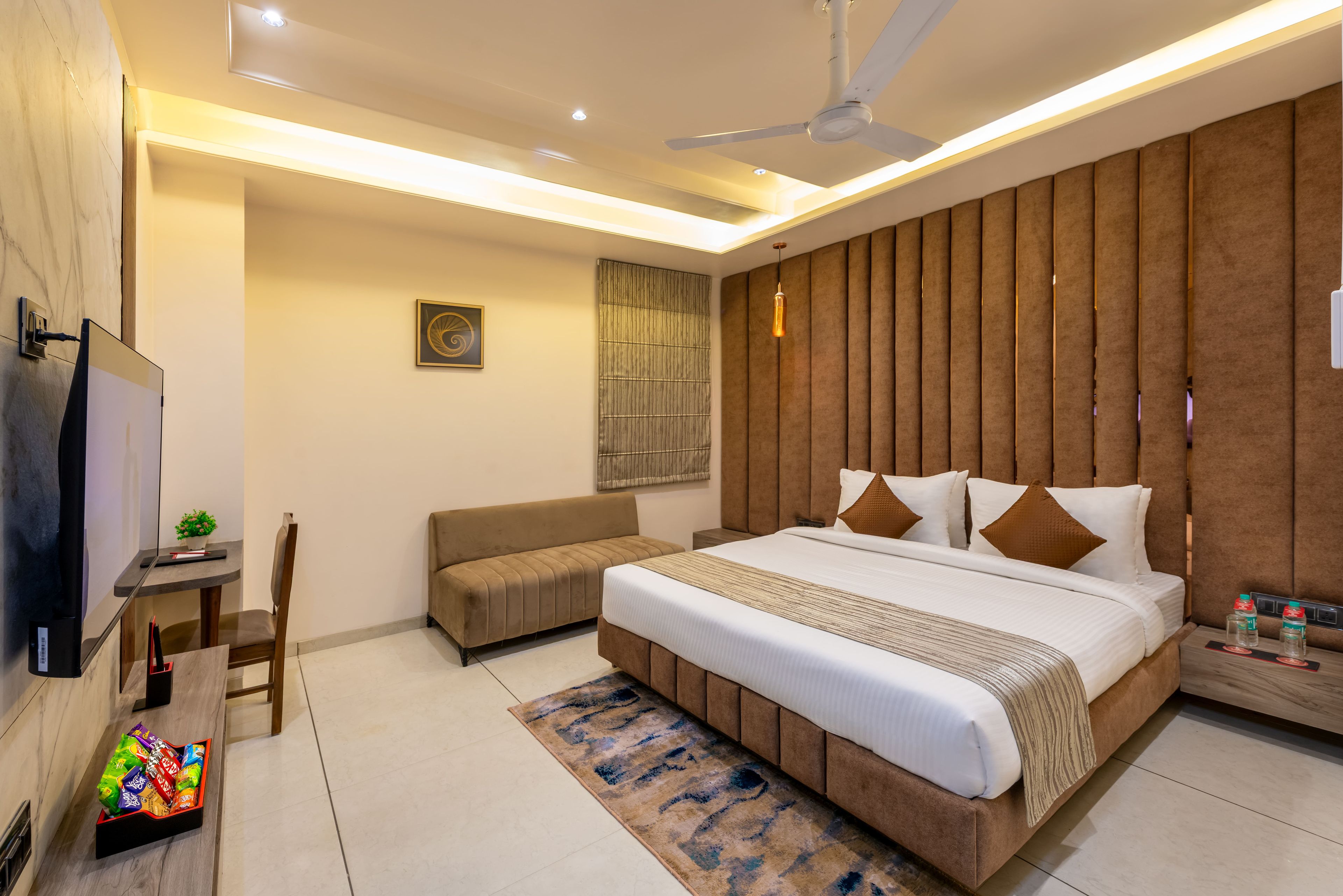 A modern hotel room with a bed, a sofa, a TV, a desk, and a ceiling fan.