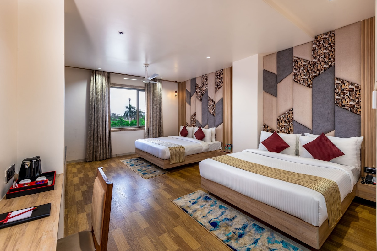 Habitación de hotel con dos camas, un escritorio con cafetera y vistas a zonas verdes.