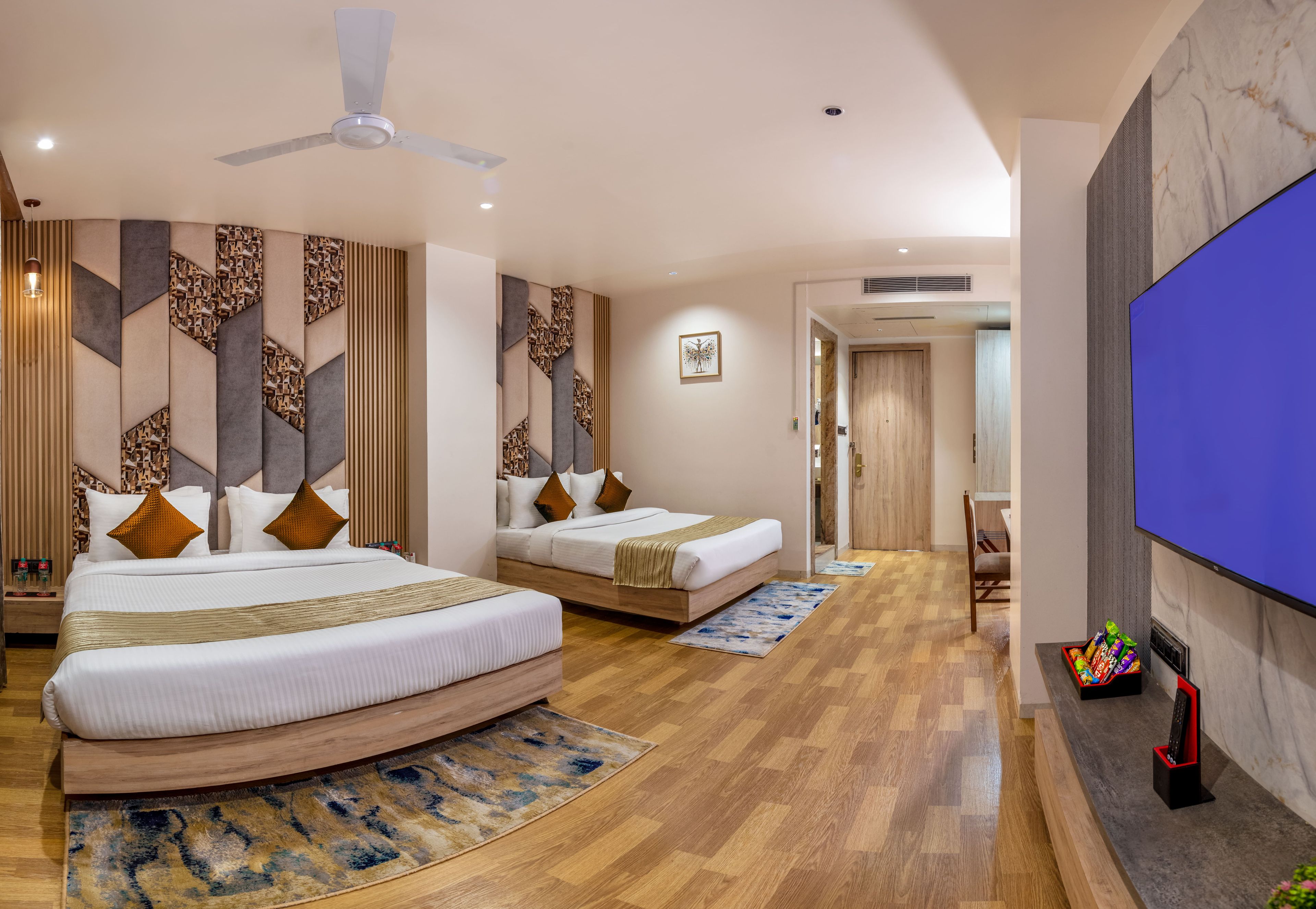 Ein Hotelzimmer mit zwei Betten, einem Deckenventilator, einem Flachbildfernseher und Holzboden.