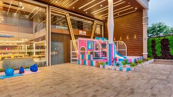 A modern hotel lobby with a play area, a reception desk, and a large glass wall.