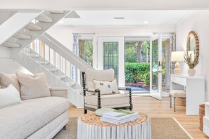 Ein modernes Wohnzimmer mit Sofa, Sessel und Couchtisch, einer Treppe und Blick ins Freie.