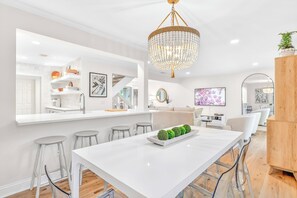 Eine moderne Küche mit einer weißen Kochinsel, Barhocker, einer Chandelierleuchtre und einem Essbereich mit weißem Tisch.