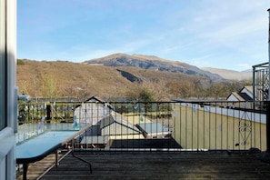Una terraza con mesa y sillas de vidrio, baranda de metal y vista a una montaña.