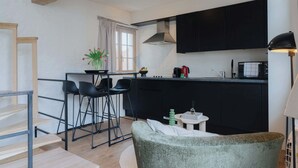 Une cuisine moderne avec des meubles de couleur noire, un coin bar avec des tabourets, une petite table agrémentée d’un vase de fleurs et une lampe.