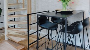 Un intérieur moderne avec un escalier en bois, une table à manger entourée de chaises noires et un vase rempli de fleurs.