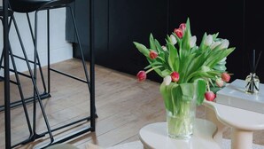 Une cuisine moderne avec des meubles noirs, un coin repas avec des chaises noires et un vase de tulipes posé sur une petite table.