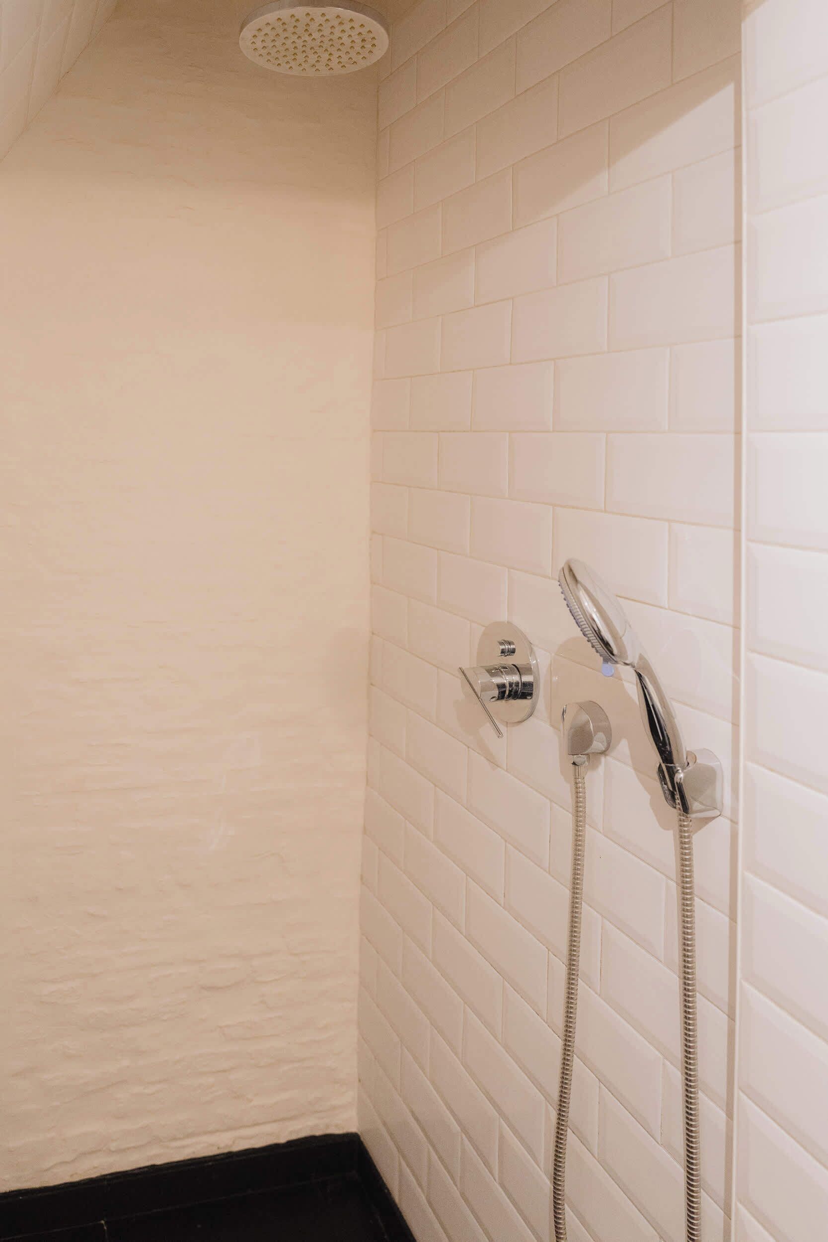 Een hoek van een kamer met witte betegelde muren, een douchekop en een slang.