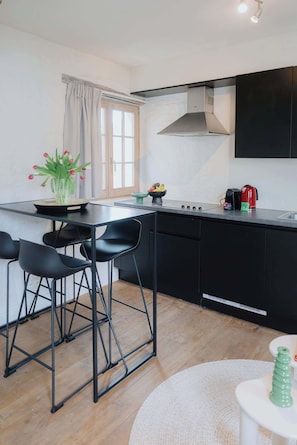 Una cocina moderna con una isla central, sillas negras, una cafetera y un ventanal con cortinas.