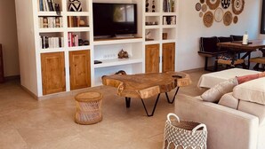 Een woonkamer met een televisie, boekenkasten, een houten salontafel, een bank en een eethoek.