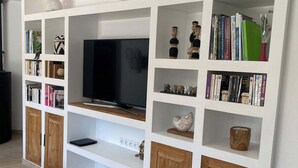 Een woonkamer met een televisie, boekenkasten, decoratieve objecten en houten kasten.