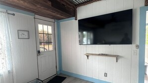 A room with a wooden ceiling, a mounted TV, a door with a window, and a black mat on the floor.