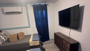A room with a bed, a TV mounted on the wall, a dresser, and an air conditioning unit.