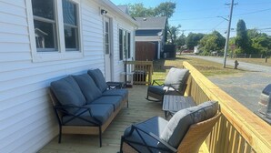 A covered porch with a sofa and chairs, a small table, and a wooden railing.