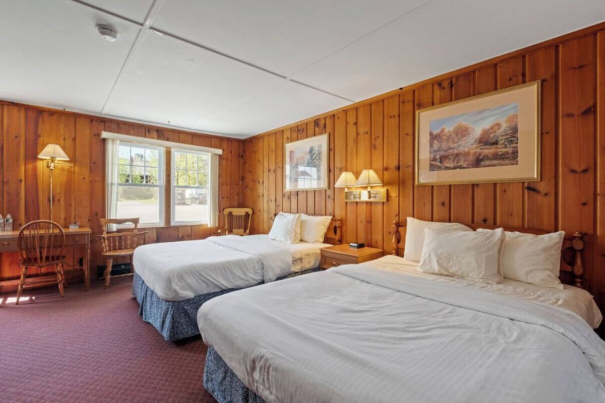 A room with two beds, wooden walls, a desk, chairs, and two lamps.