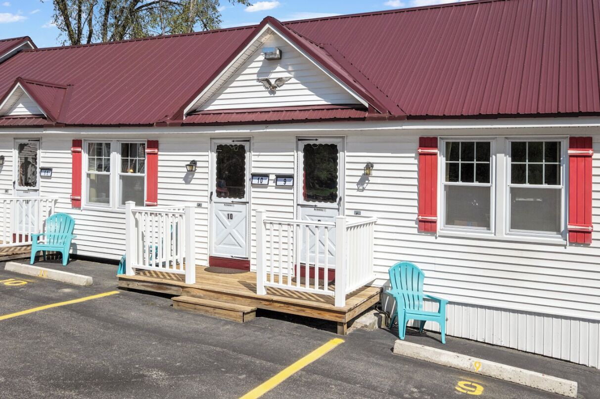 A row of white cabins with red shutters, numbered 10 and 9, and a wooden deck with chairs.